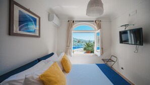 A hotel room with a bed, a television, a window with curtains, and a view of the sea. - Villa Margherita by My Villa Collection (Anacapri)