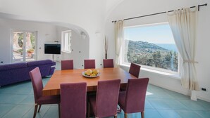 A dining area with a wooden table and purple chairs, a sofa, and a TV. - Villa Margherita by My Villa Collection (Anacapri)