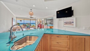 Une cuisine moderne avec un plan de travail turquoise, un évier en acier inoxydable, des armoires en bois et un ventilateur de plafond.