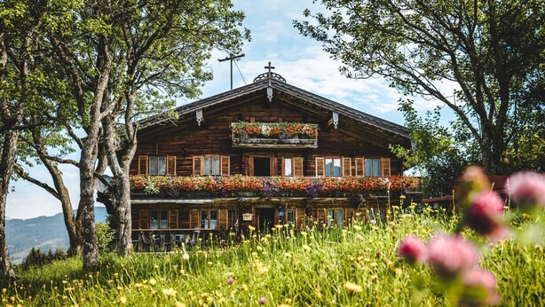 A wooden building with a balcony, surrounded by lush greenery and flowers. - Beautiful Apartment in Tyrol With Terrace (Westendorf)