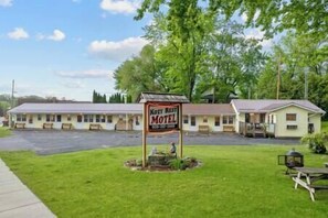 A motel with a sign reading "Koxx Rest Motel" in front of a row of single-story buildings with a parking lot in front.