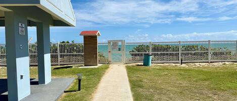 A pathway leading to a building with a red roof, a fenced area with a gate, and a clear sky.
