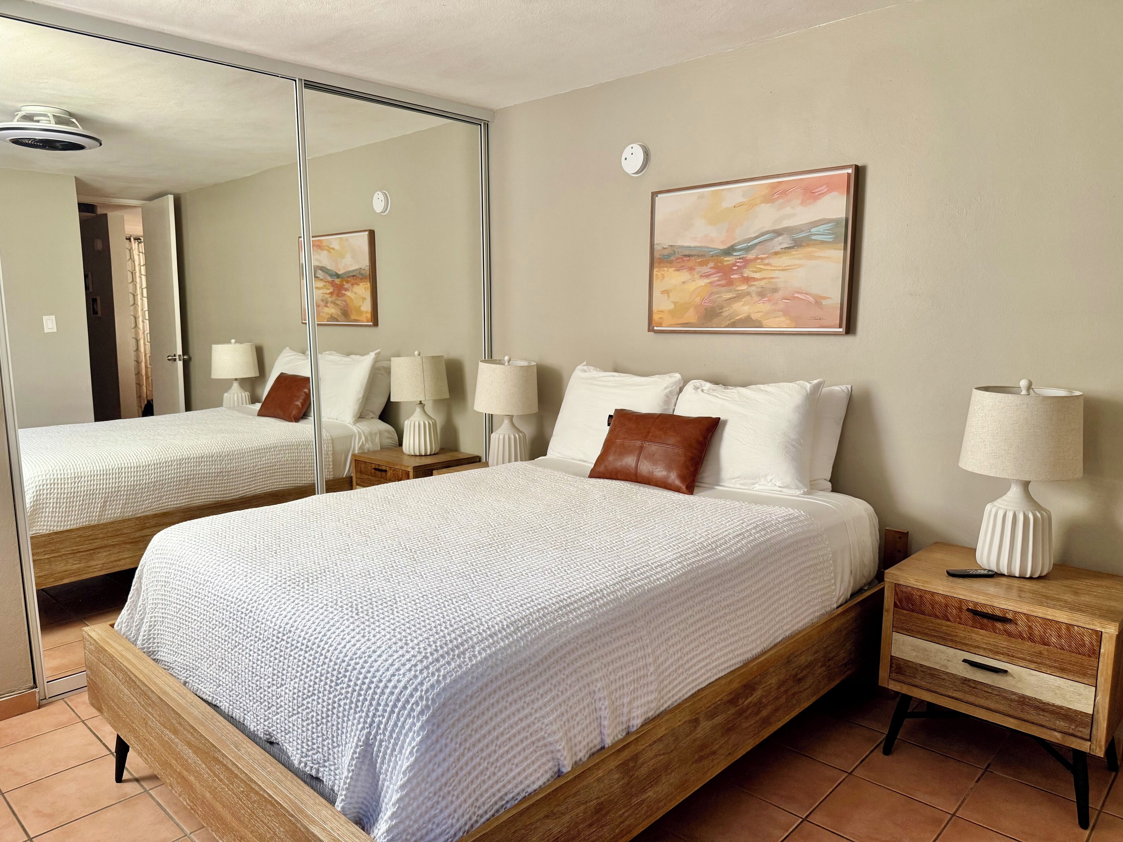 A hotel room with a large bed, two bedside tables, a mirror, and a painting on the wall.