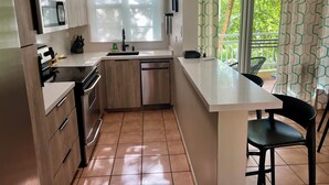 Una cocina compacta con microondas, estufa, lavamanos y un pequeño comedor con una silla.