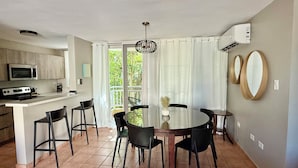Cocina moderna con microondas, estufa y barra. Hay una mesa de comedor con sillas y vistas a zonas verdes.