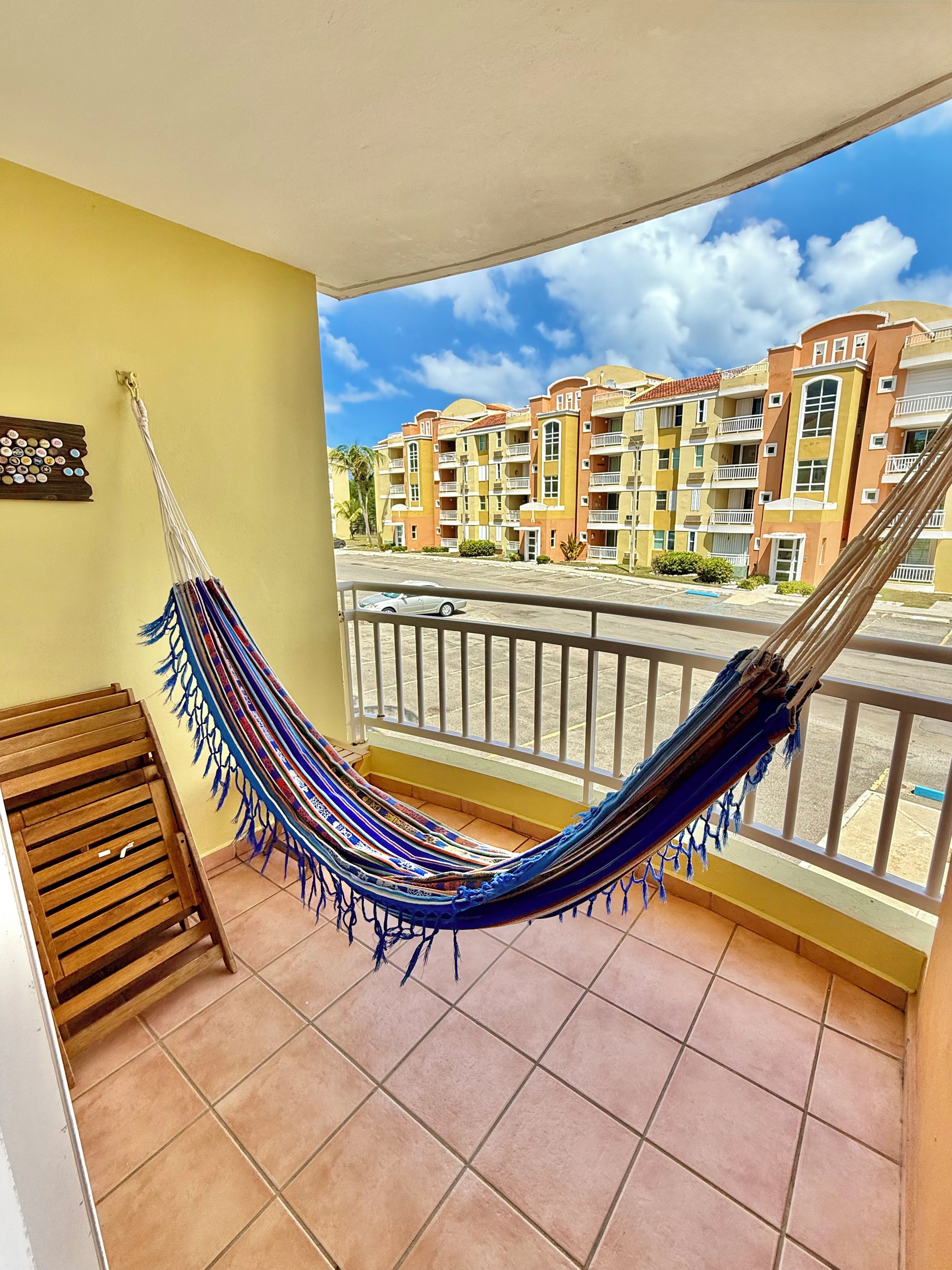 A room with a hammock, a wooden bench, and a view of a residential area with multi-story buildings.