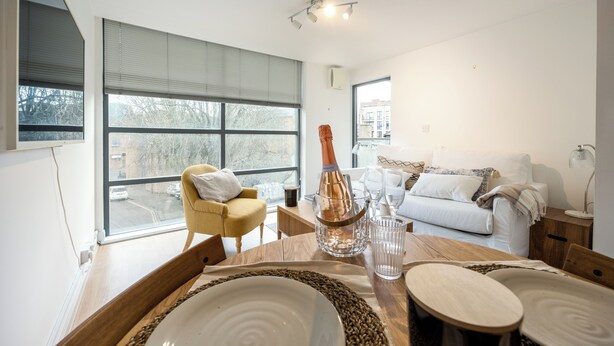 A modern living room with a dining area, large windows, a sofa, and a table set for a meal. - Modern Flat, Oxford city centre (Oxford)