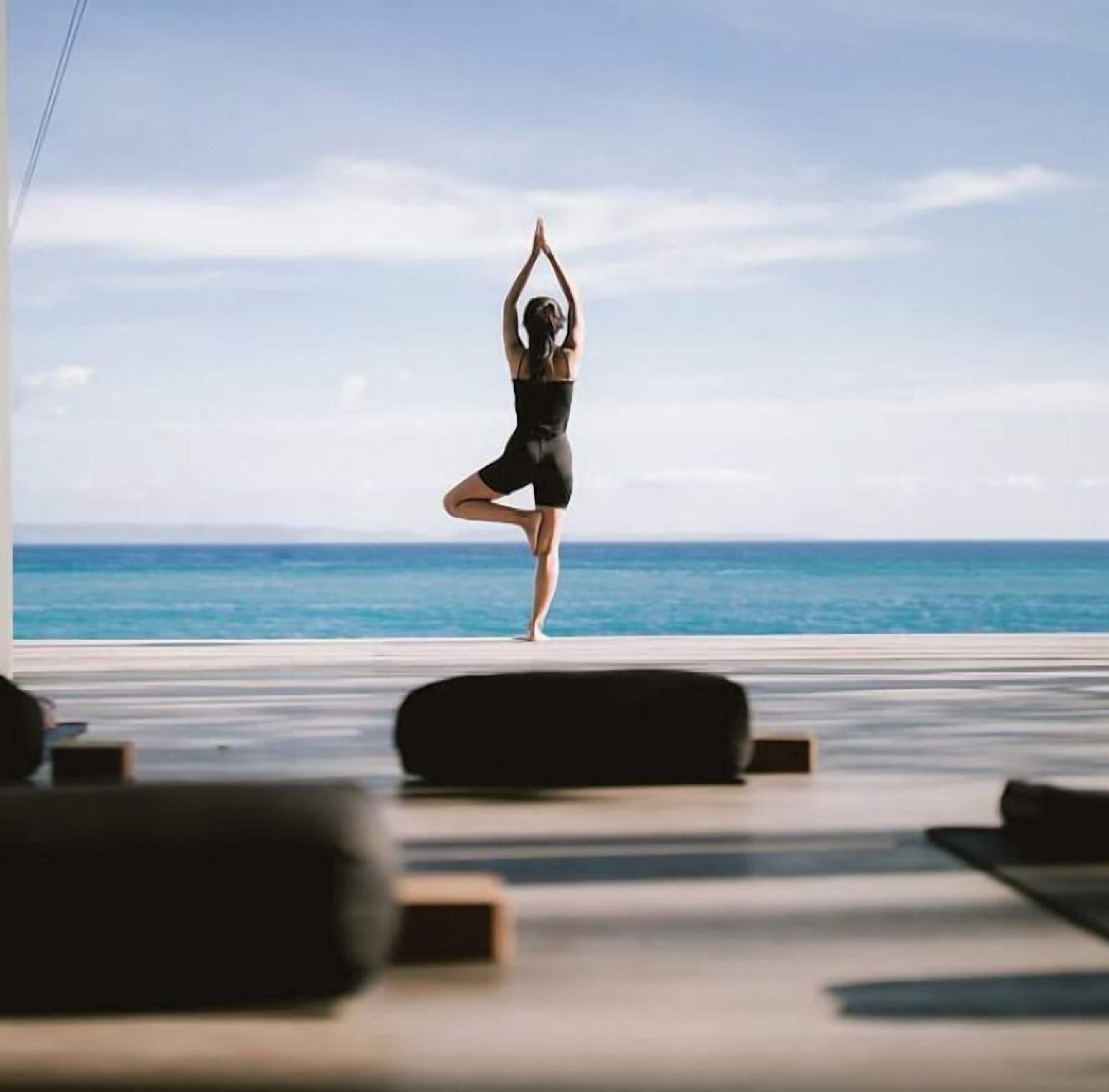 A person performing a yoga pose on a balcony with a view of the ocean.