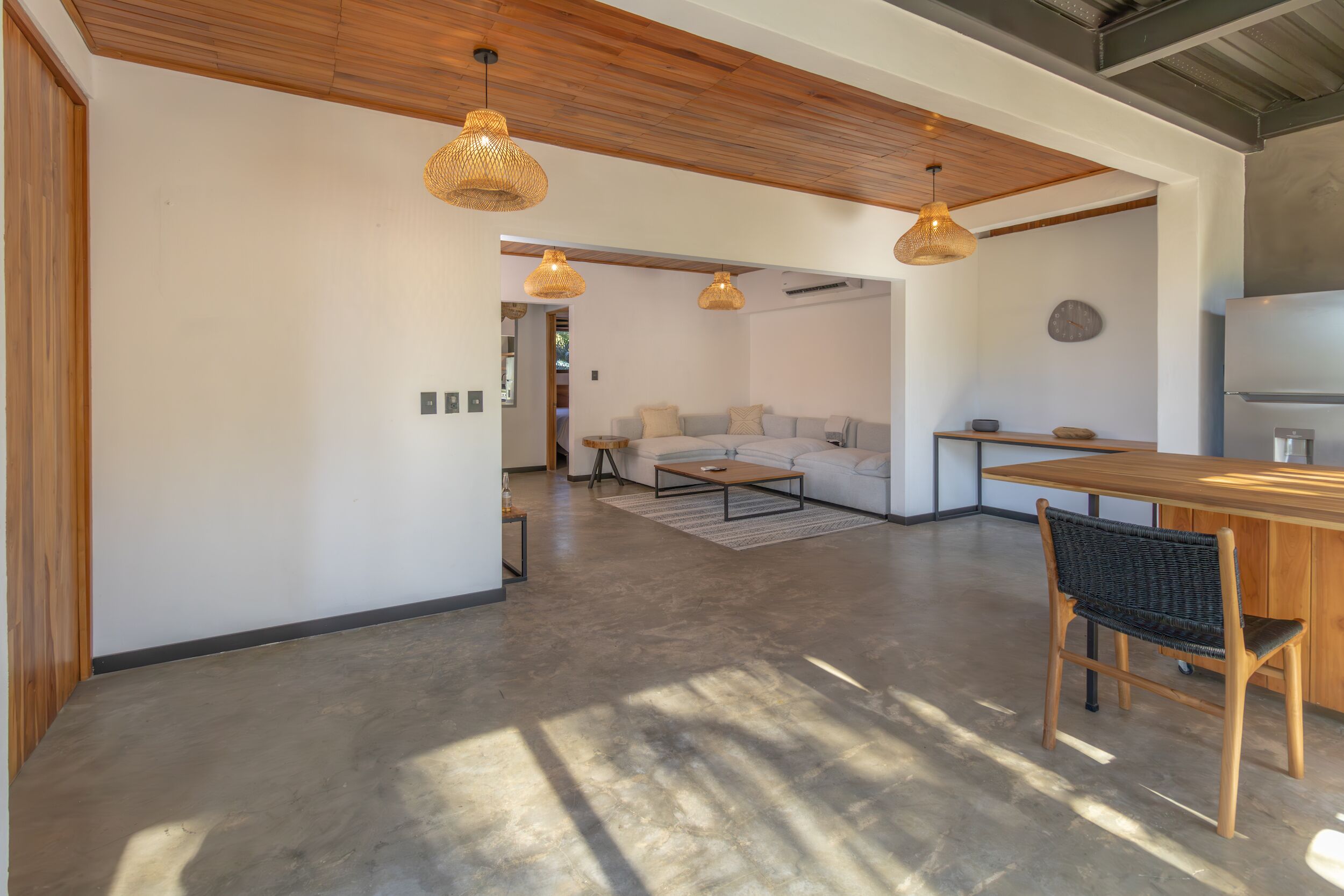 Ampla sala de estar com teto de madeira, um sofá, mesa de centro e uma mesa de jantar com cadeiras.