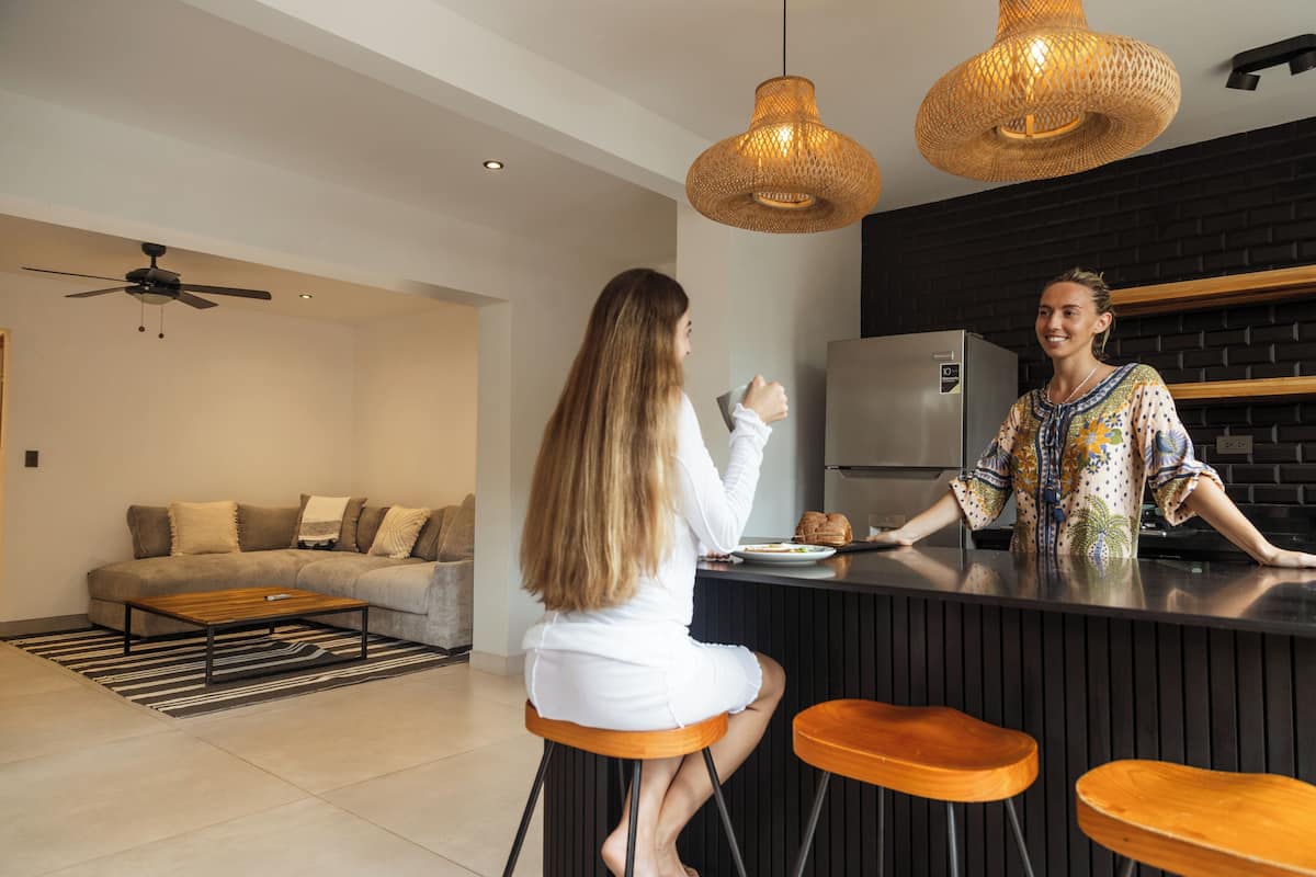 Una cocina moderna con encimera negra, dos taburetes de madera y una lámpara colgante.