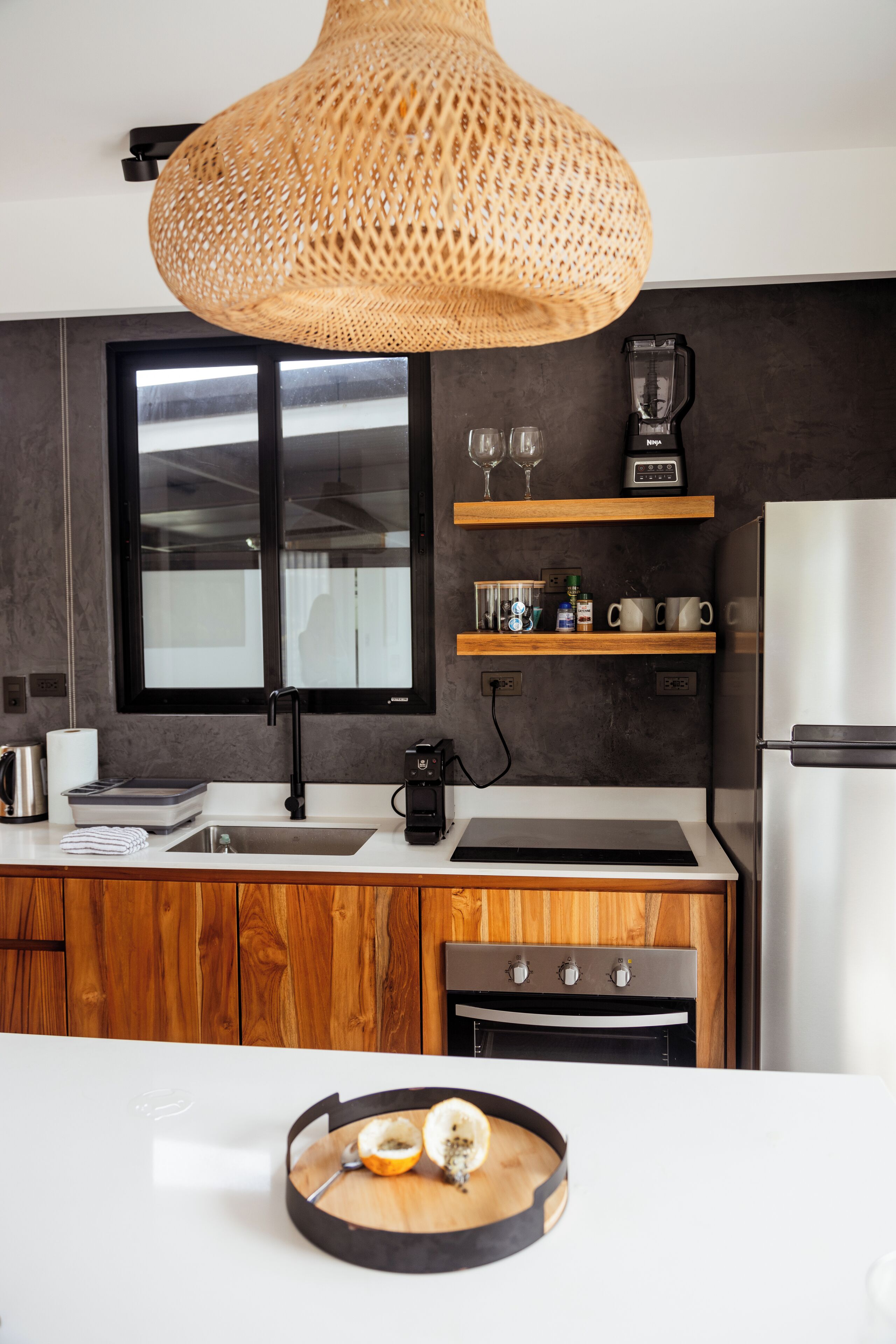 Een moderne keuken met een groot raam, houten kastjes, een ingebouwde oven en een wit aanrecht.