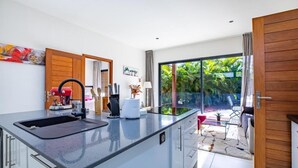 Una cocina moderna con una isla grande, una cafetera y vistas a un jardín exuberante a través de un ventanal corredero.