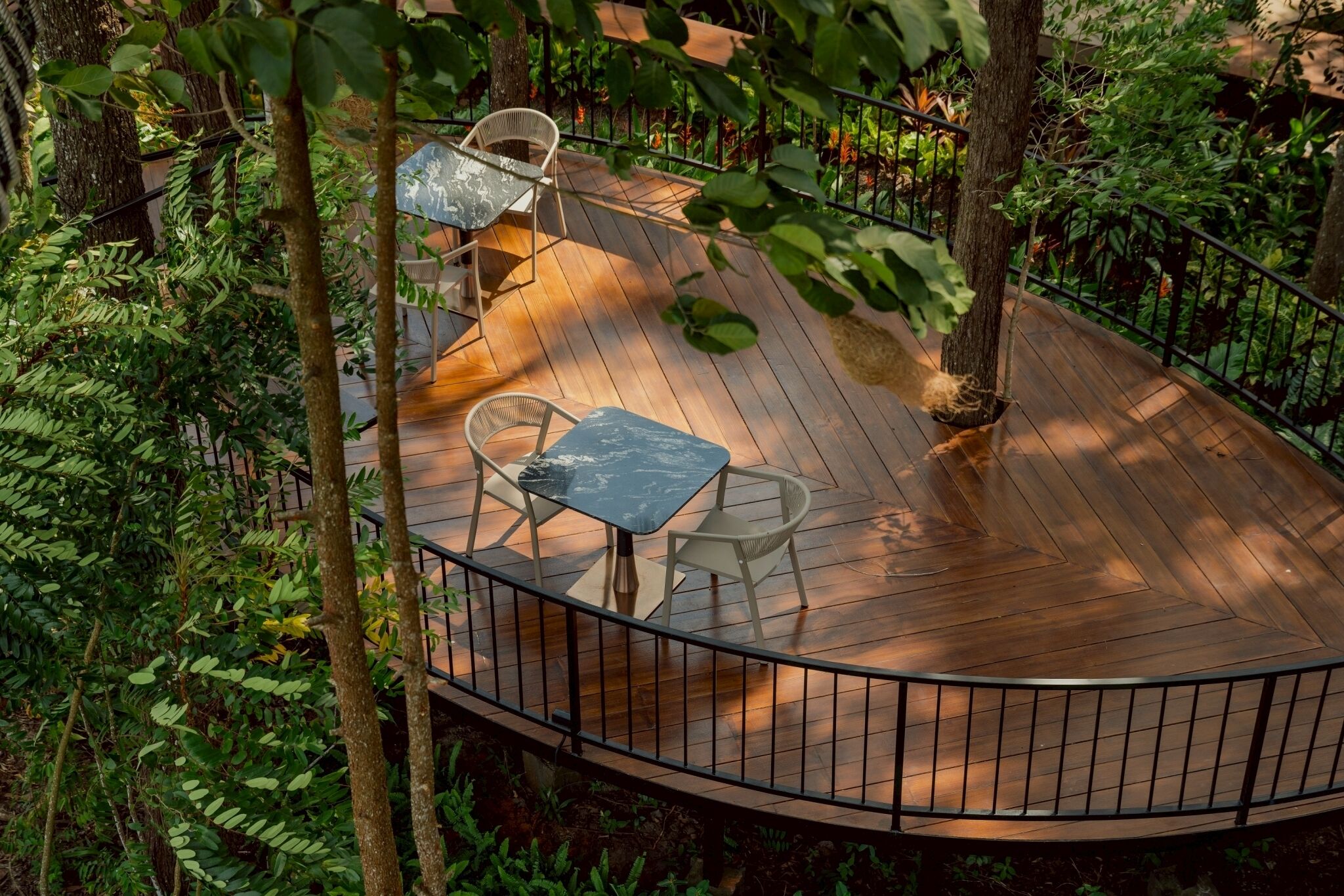 Una terraza de madera con barandilla curva, rodeada de abundante vegetación.