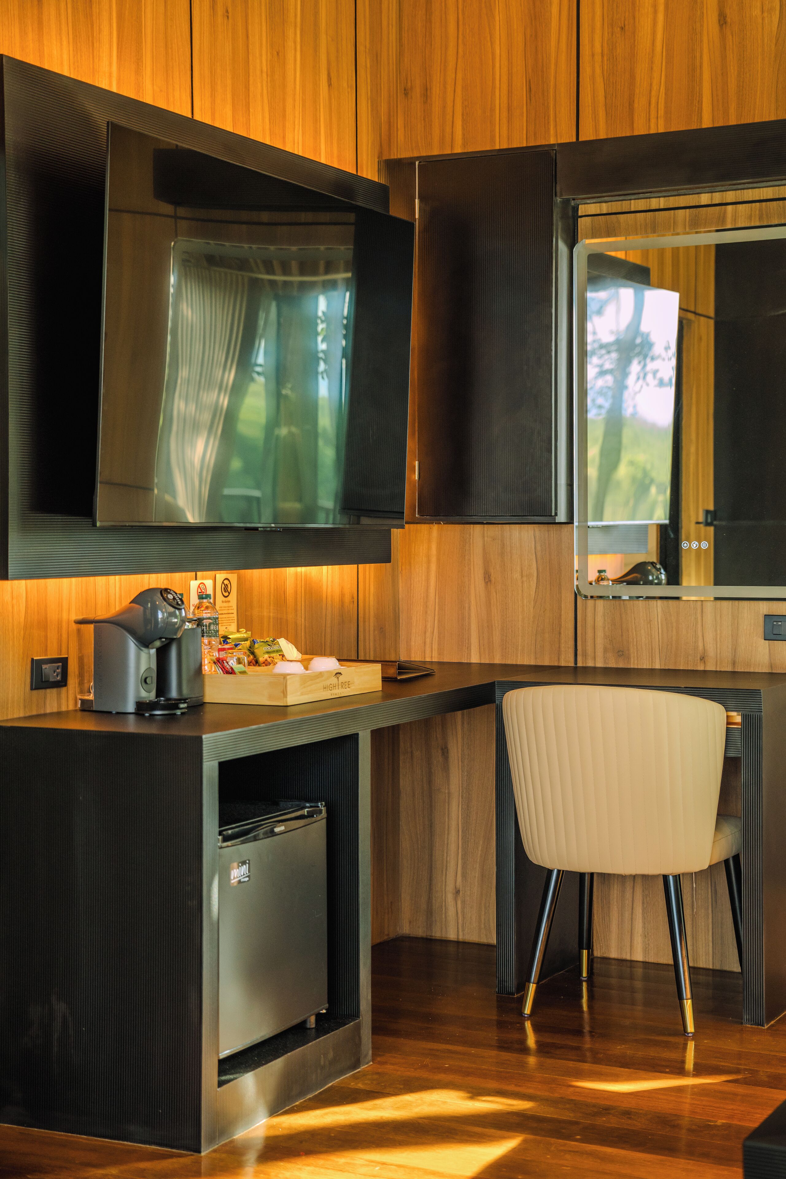 A modern kitchen with wooden cabinetry, a built-in refrigerator, a coffee machine, and a seating area with a chair.
