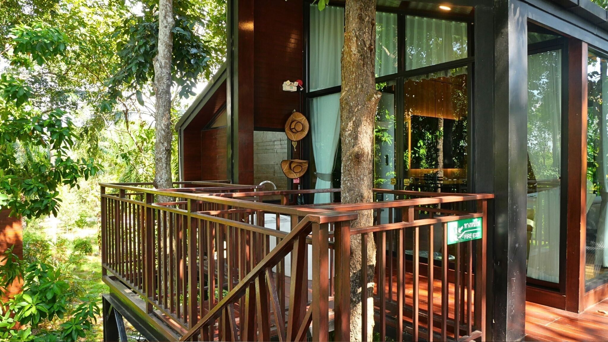 A wooden deck with a railing, a fire exit sign, and a view of the surrounding greenery.