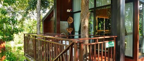 A wooden deck with a railing, a fire exit sign, and a view of the surrounding greenery.