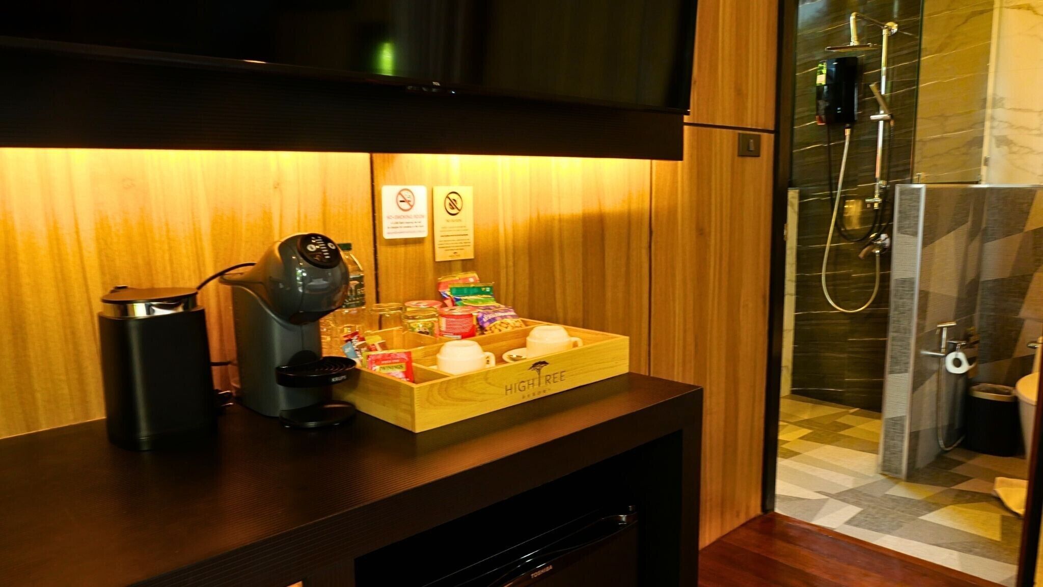 A wooden counter with a coffee machine, a tray of snacks, and a shower area with a glass door.
