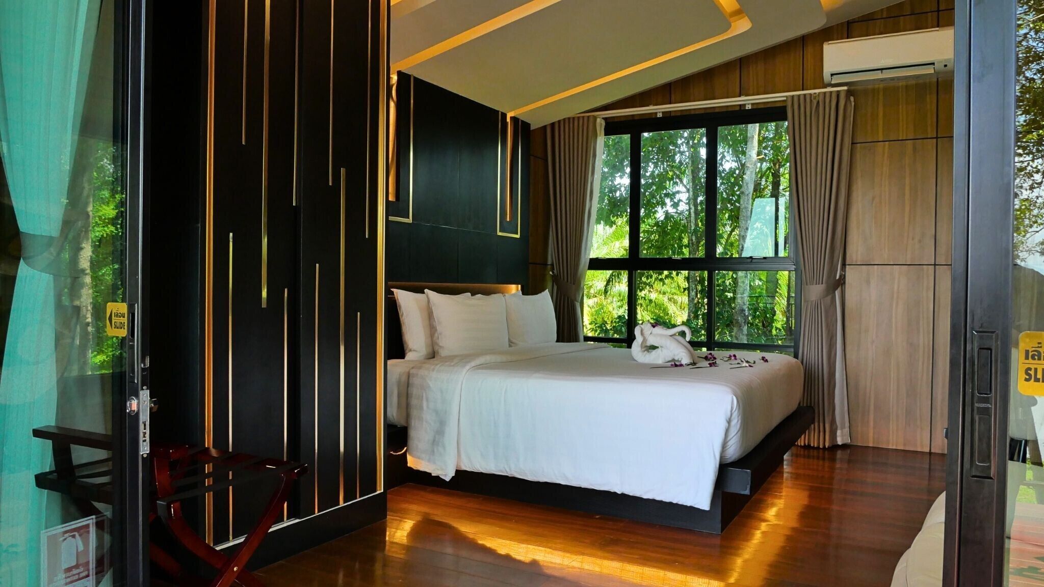 Ein modernes Hotelzimmer mit einem großen Bett, einem Fenster mit Blick auf Grünflächen und einer Schiebetür.