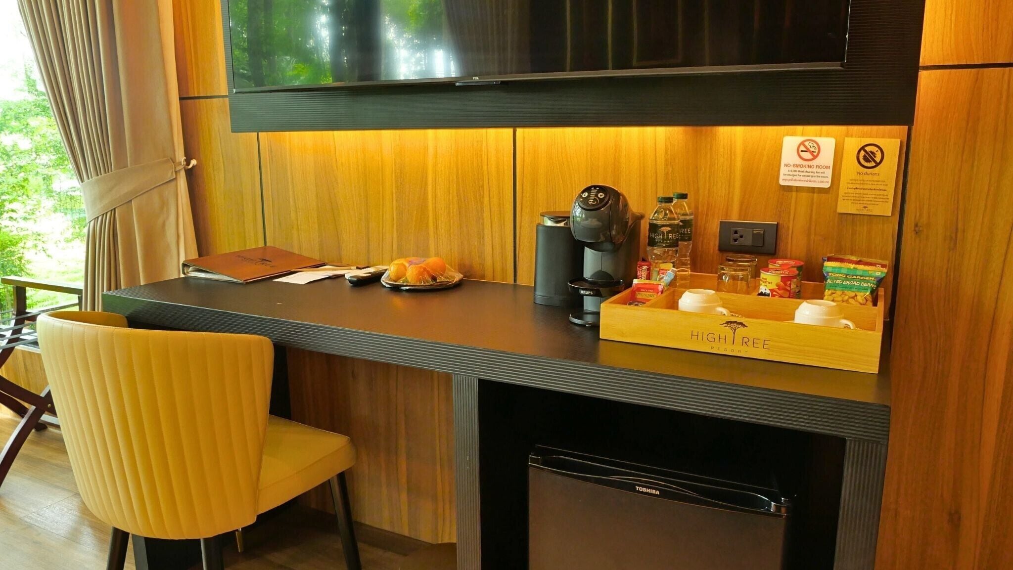 Una cocina compacta con televisor de pantalla plana, cafetera y refrigerador pequeño.