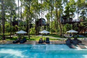 A pool with lounge chairs and umbrellas, surrounded by trees and forest. - High Tree Resort Co.,Ltd. (Krabi)