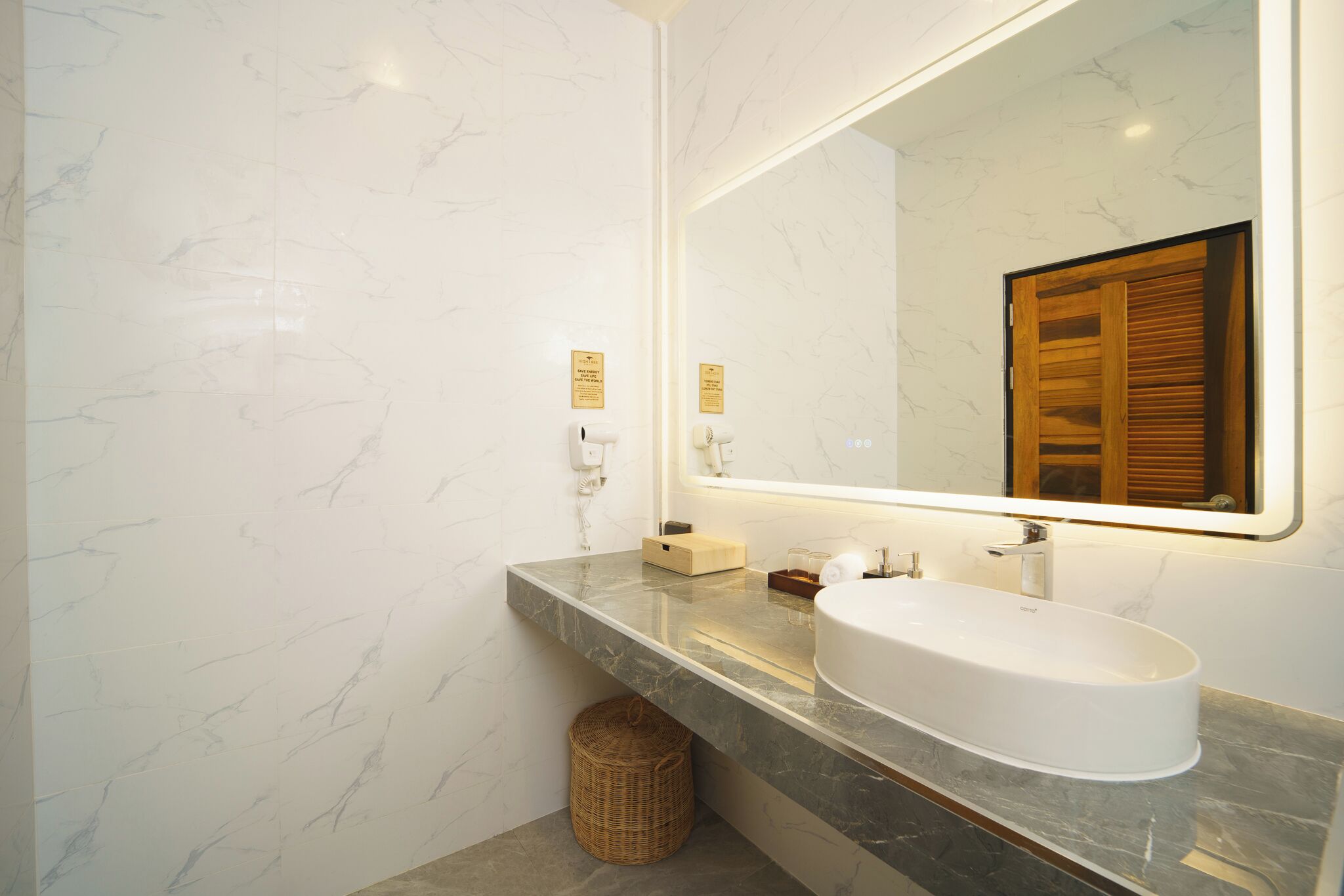 Une salle de bain moderne avec un mur en marbre, un grand miroir, un lavabo blanc et un meuble-lavabo en bois.