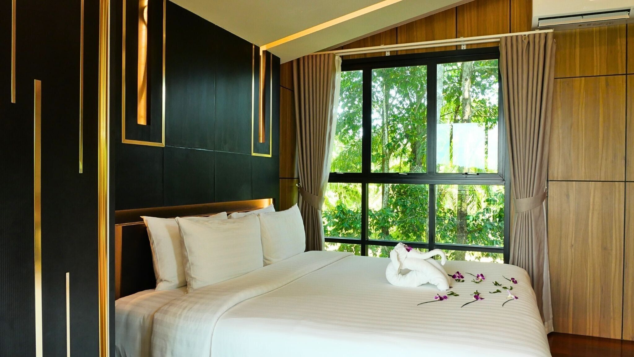 Een hotelkamer met een groot bed, uitzicht op groen door het raam, en een modern design met donkere wanden en gouden accenten.