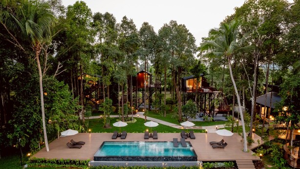 A pool area with lounge chairs and umbrellas, surrounded by trees and a wooden deck.