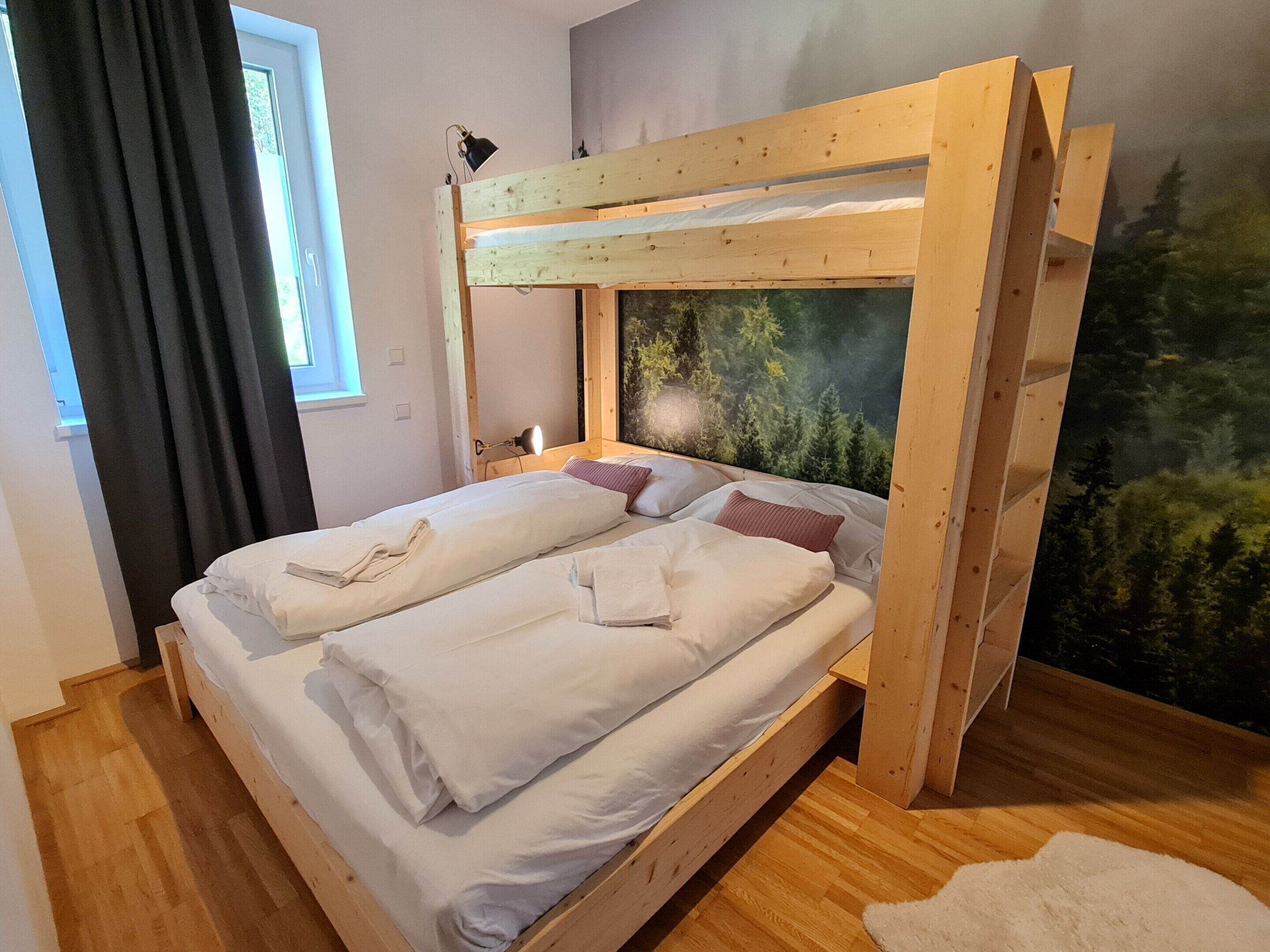 A bunk bed with white bedding and a forest mural on the wall.