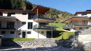 Un immeuble résidentiel moderne à plusieurs étages, doté de balcons, d’un mur de soutènement en pierre et d’un espace de stationnement.