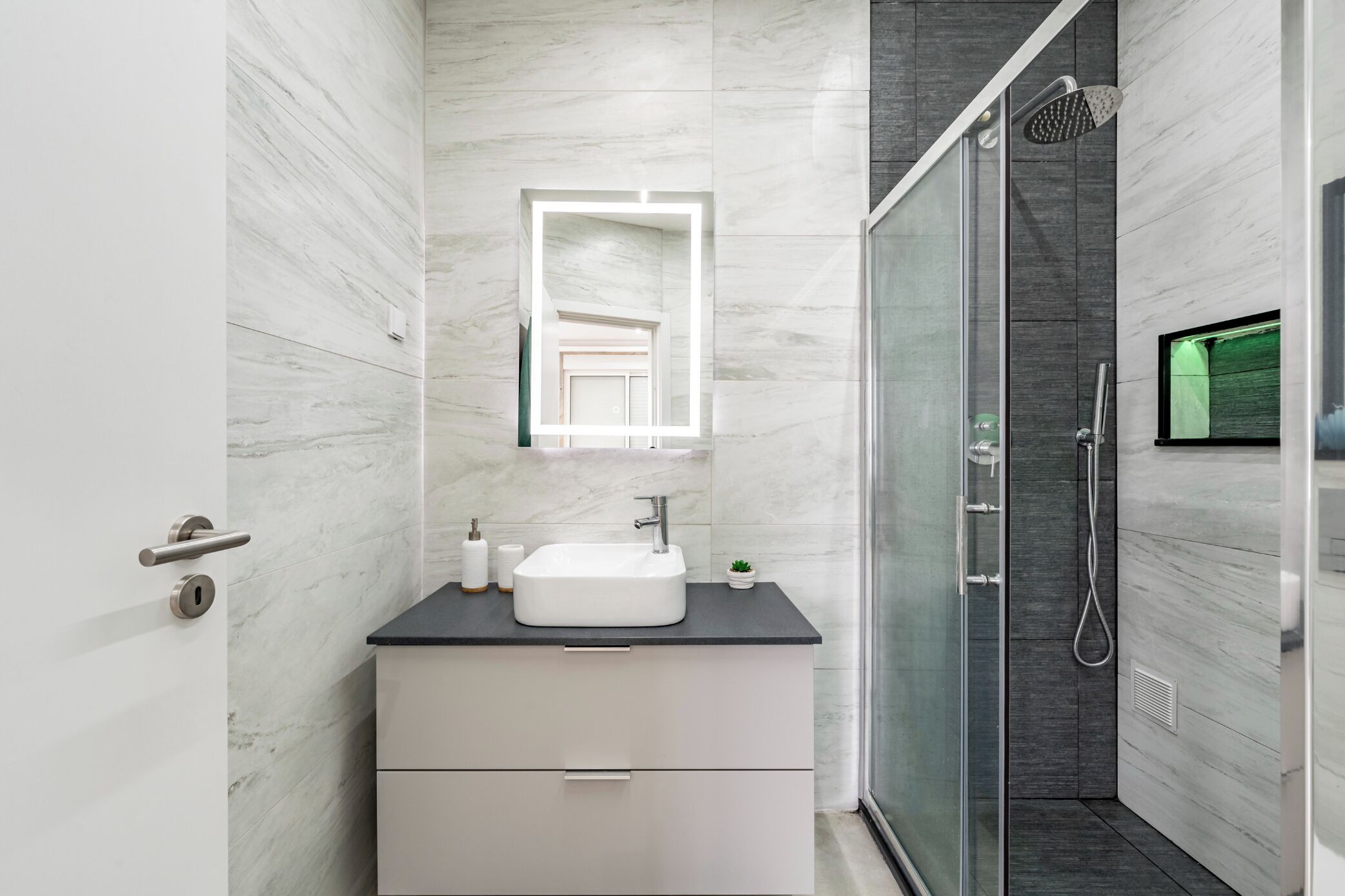 A modern bathroom with a white vanity, a glass shower enclosure, and a marble wall.