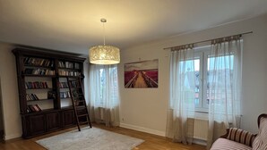 A spacious living room with hardwood flooring, a large bookshelf, a ladder, a sofa, and a hanging light fixture. - Stadthotel Reckers (Werne)