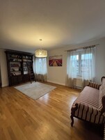 Un salón amplio con suelo de madera, una gran estantería, una escalera, un sofá y una lámpara colgante.