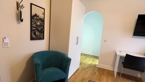 A compact room with a teal armchair, a white wardrobe, a desk, and a television. - Stadthotel Reckers (Werne)