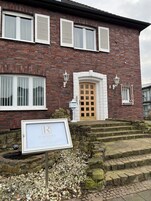 Un edificio de ladrillo con puerta de madera y varias ventanas, una escalera de piedra y un cartel.
