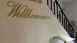 A staircase with a wall sign that reads "Herzlich Willkommen" in gold lettering. - Stadthotel Reckers (Werne)
