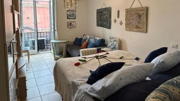 A cozy room with a bed, a small table, and a sofa. There is a window with a view of buildings outside. - Apartment sea view GAETA (Gaeta)