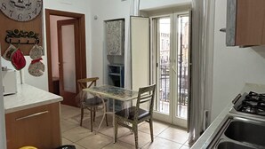 A small kitchen with a table and chairs, a sink, and a window with a view of buildings. - Apartment sea view GAETA (Gaeta)