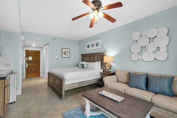 A bedroom with a bed, a wooden headboard, a nightstand with a lamp, a sofa, and a ceiling fan.