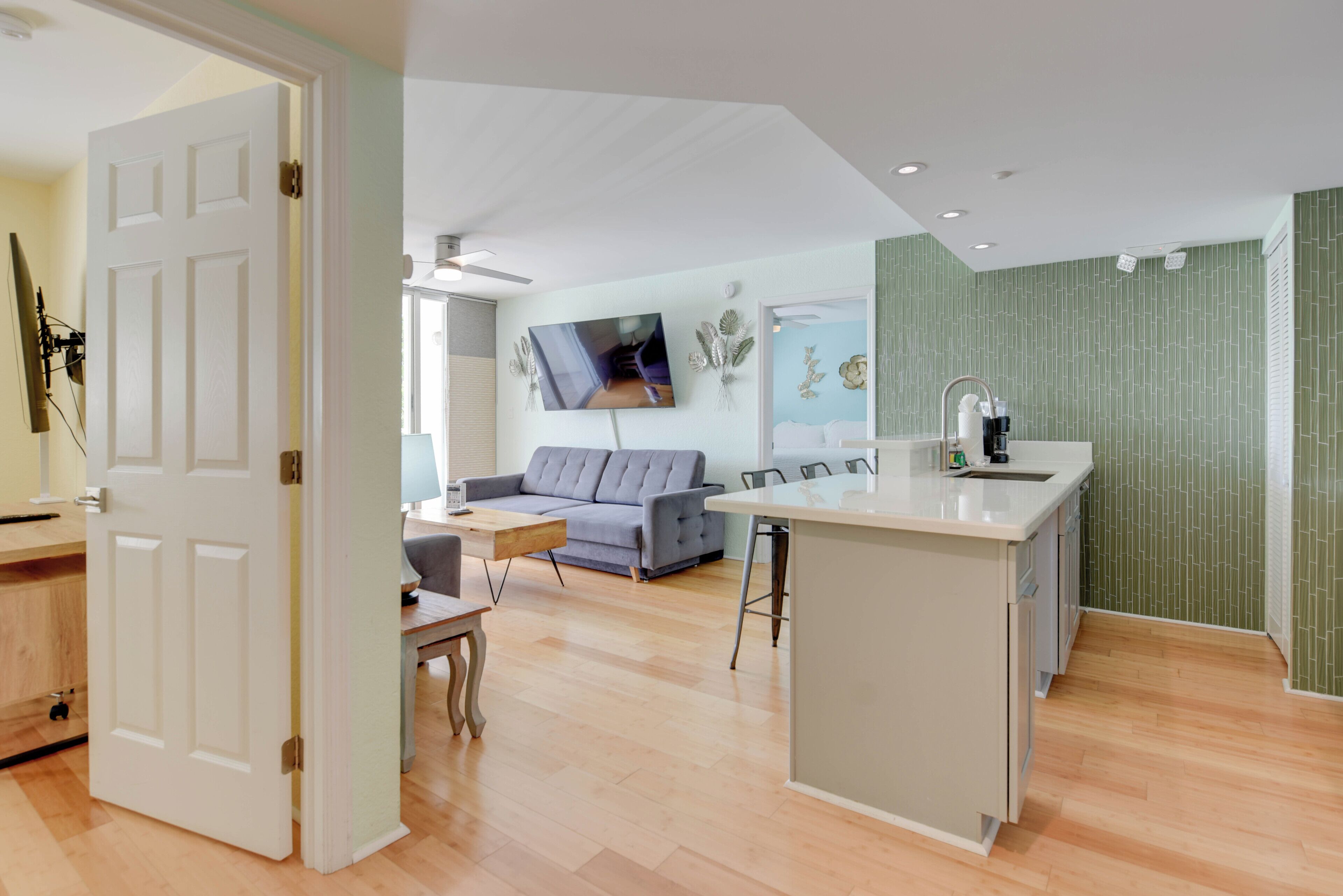 Una cocina moderna con una isla central, un comedor con un sofá gris y una sala de estar con televisor de pantalla plana.