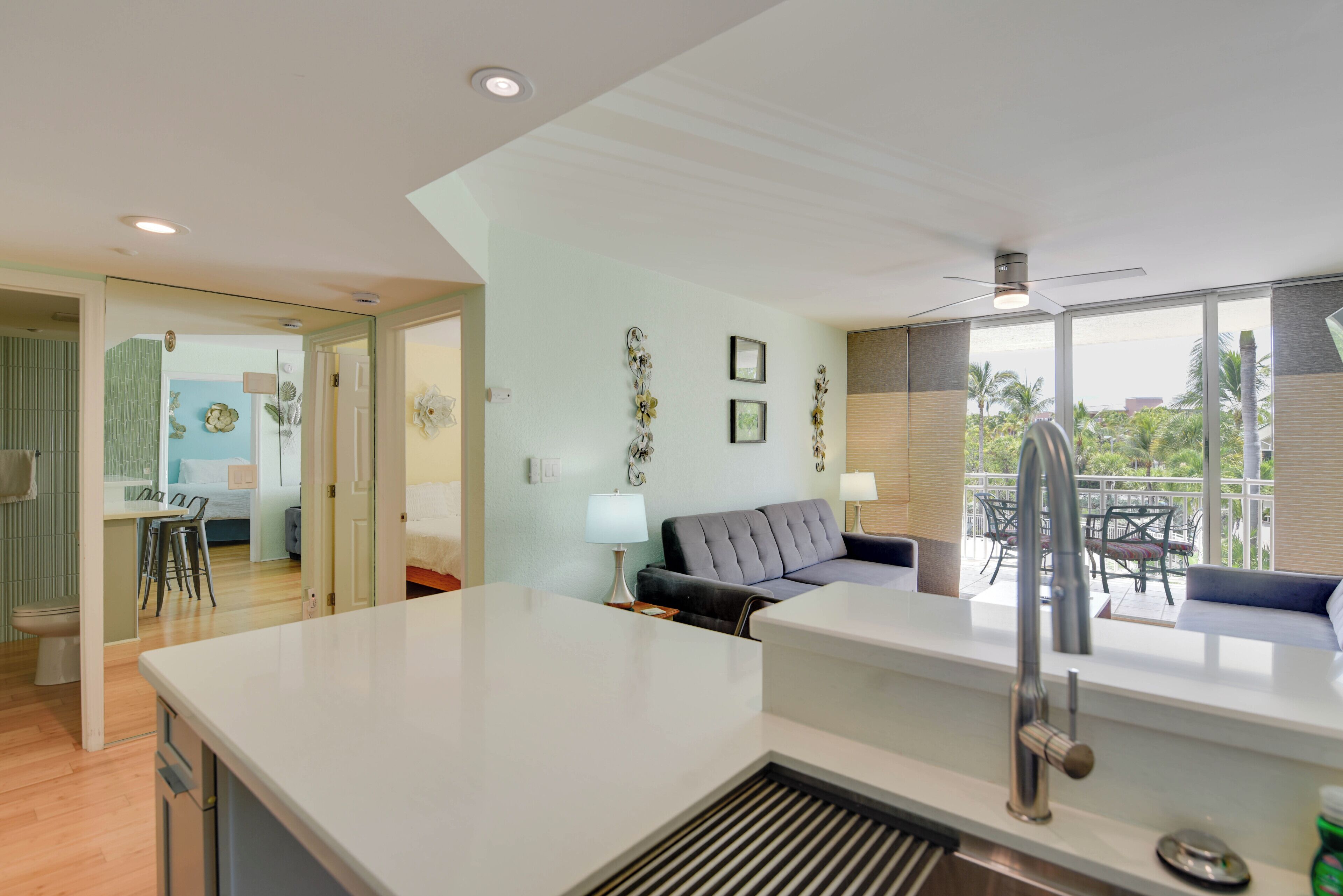 A modern kitchen with a central island, a dining area with a sofa, and a view of the outdoors through large windows.