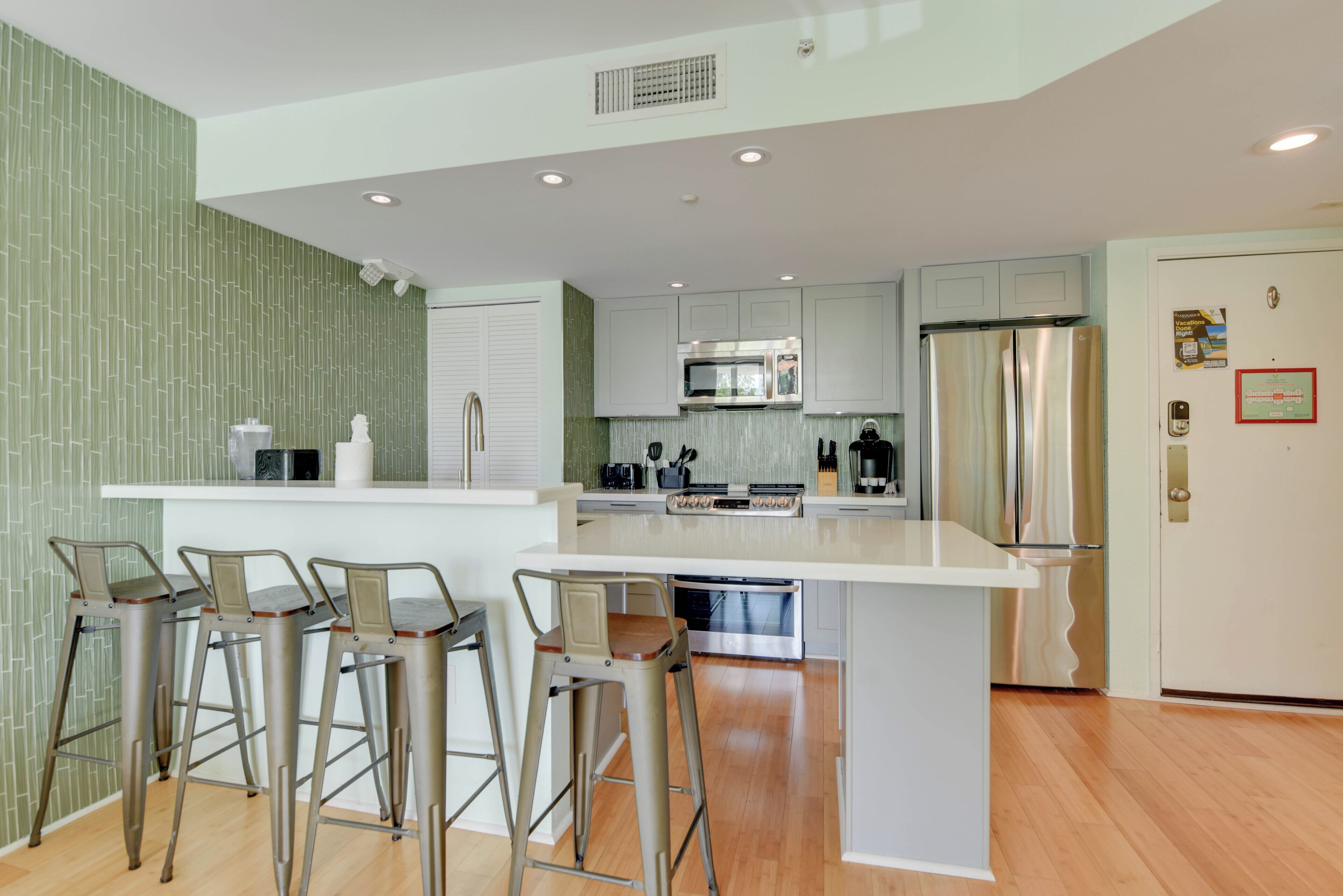 Una cocina moderna con una isla central, taburetes de bar, electrodomésticos de acero inoxidable y un salpicadero con estampado verde.