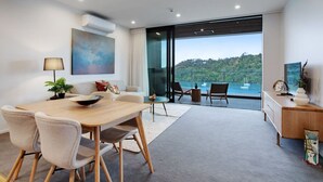 A modern living room with a dining area, large windows, and a view of the sea. - Catalina Bay Seascape with Bay Views and Carpark (Auckland West)