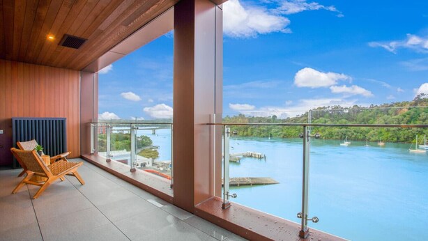 A balcony with a view of a river and boats, wooden chairs, and a glass railing. - Catalina Bay Seascape with Bay Views and Carpark (Auckland West)