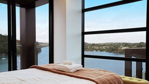 A hotel room with a large window offering a view of a body of water and a distant landscape. - Catalina Bay Seascape with Bay Views and Carpark (Auckland West)