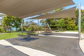 An outdoor seating area with a shaded canopy, picnic tables, and a playground structure.