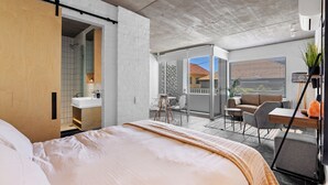 A modern bedroom with a large bed, a bathroom with a sink, and a balcony with seating. - Seaside Studio Perfect Location (Cape Town)