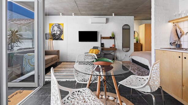 A modern living room with a glass table, white chairs, a sofa, and a TV. - Seaside Studio Perfect Location (Cape Town)