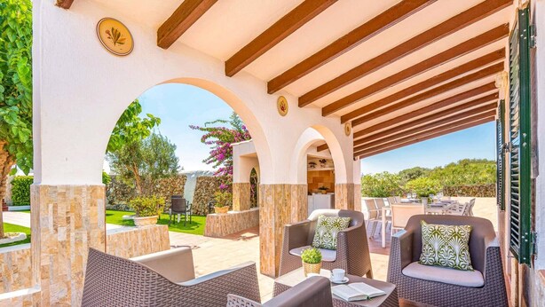 An outdoor patio area with wicker furniture, stone pillars, and a view of the surrounding landscape. - Villa Verde Ciutadella by Villa Plus (Ciutadella de Menorca)