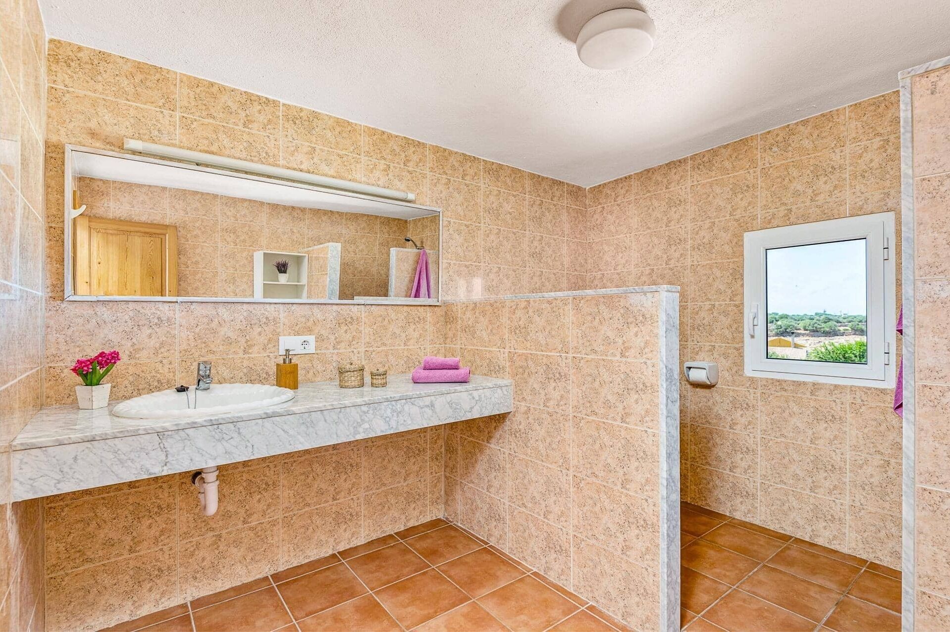 Un baño con lavamanos de mármol, un espejo, una ventana con vistas y zona de ducha.
