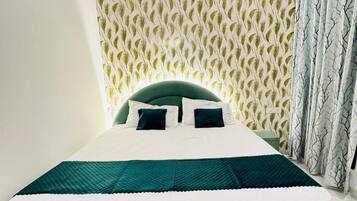 A bed with a green headboard and white bedding, a patterned wallpaper, and a curtain with a tree design.